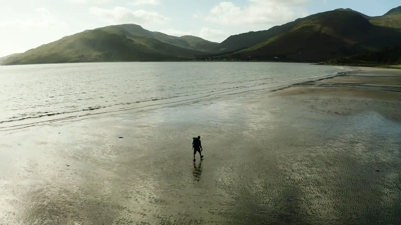 Aerial View Of Sillhoutte Of Backpacker Walking Along Beach At Glenelg With Isle of Skye In Background Scotland