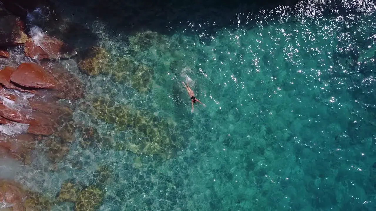 Aerial top down shot of woman swimming in clear turquoise water