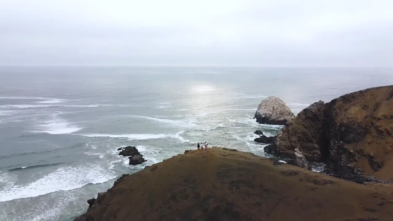 Group of friends on top of a hill with a stunning view of the ocean cliffs and sun in a beach in Peru