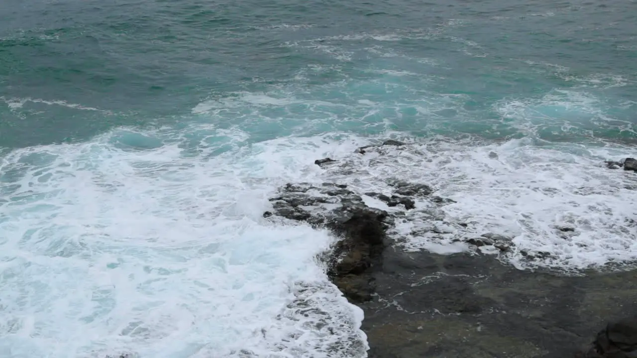 Waves crashing into a rocky formation near the shoreline of a large wave breaking on stones to the sides captured at normal speed at 24fps