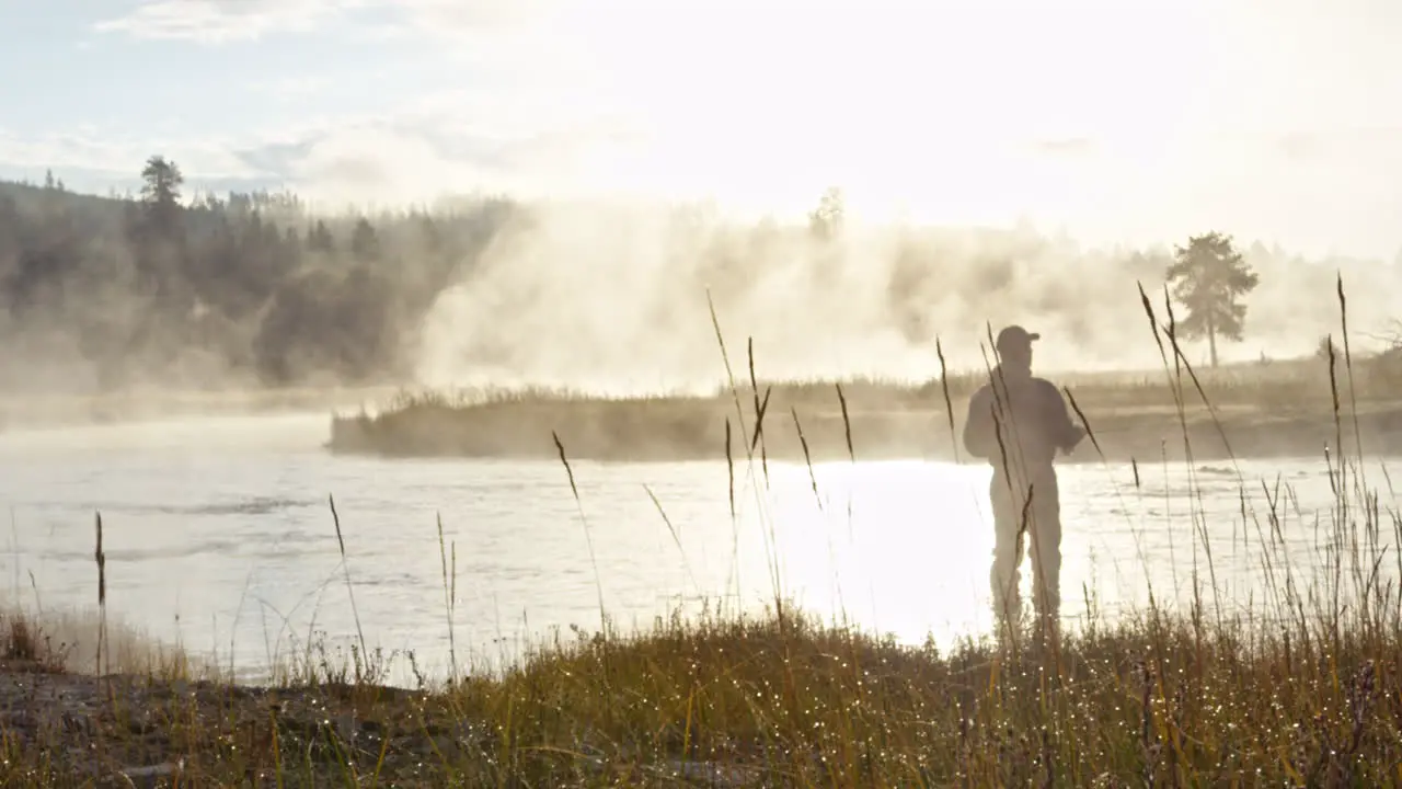 Silhouette of a fisherman fishing in a river during misty in the morning