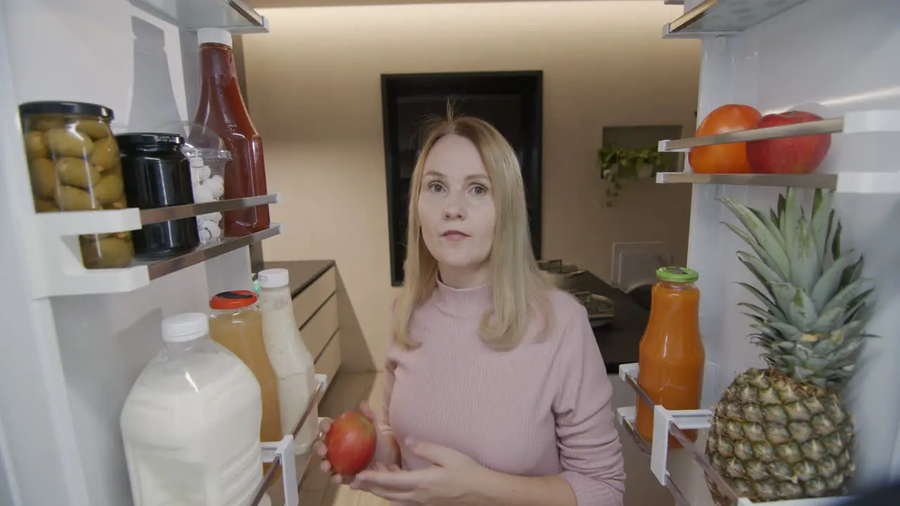 The woman takes an apple from the refrigerator Light snack view from inside the refrigerator