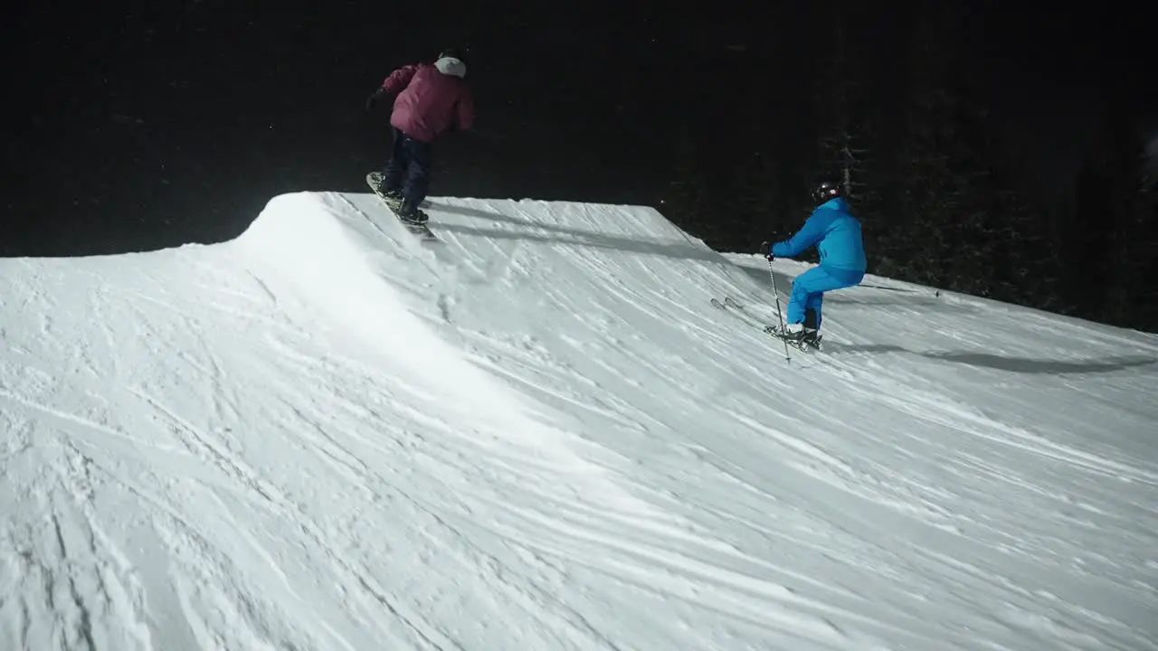 4K slow motion tracking at night of skier and snowboarder jumping on snow hill in the dark at ski resort in Norway