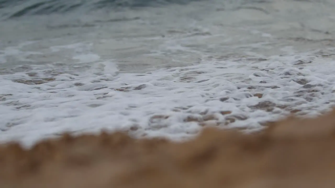 Dramatic close up of waves landing on beach with sand in foreground