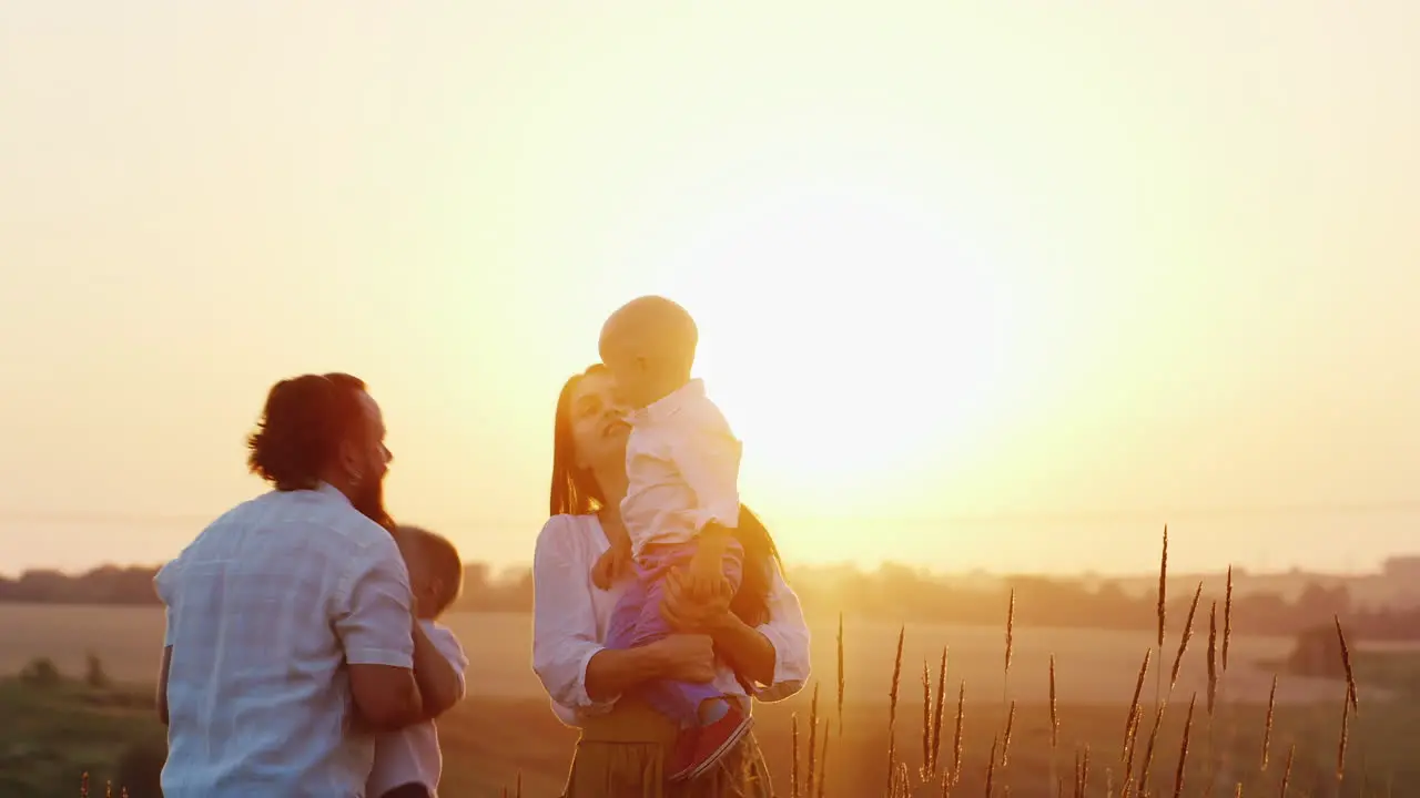 Young Family With Two Children Playing On Nature On The Sunset