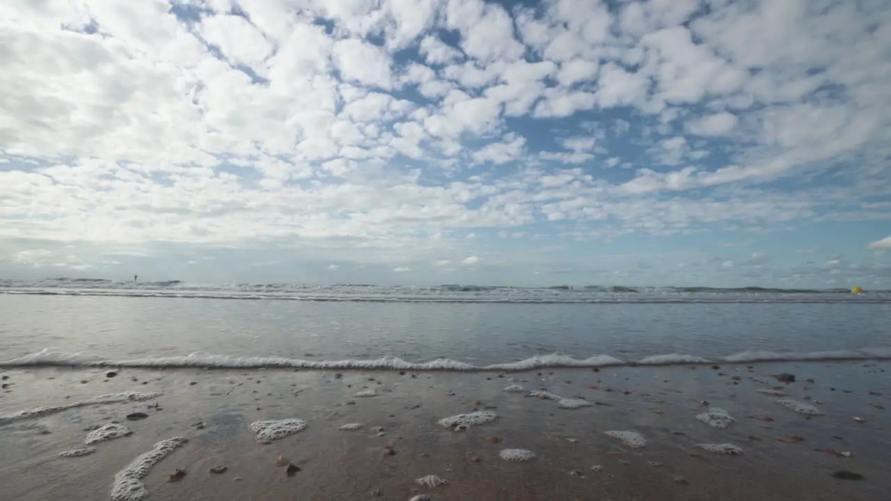 Closeup of small waves washing gently onshore high stratus clouds on the horizon North Sea Belgian coast