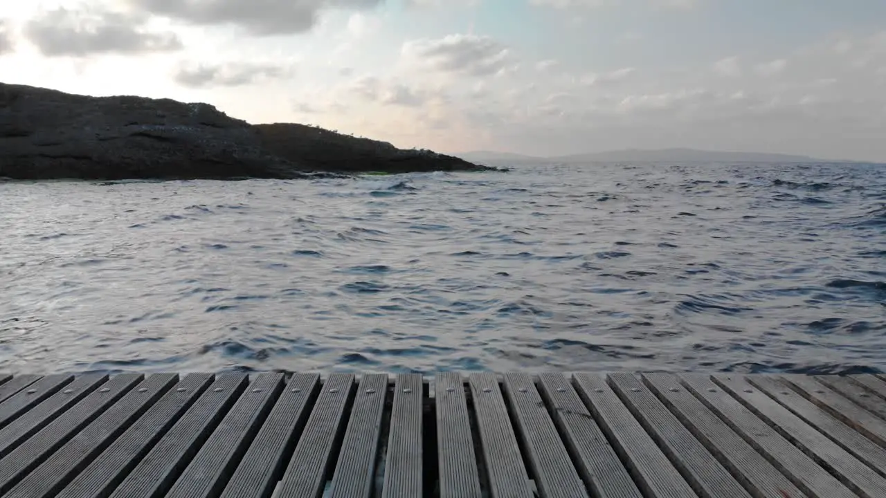 The shot is moving horizontally along wood pier from the shore to the sea in sunset