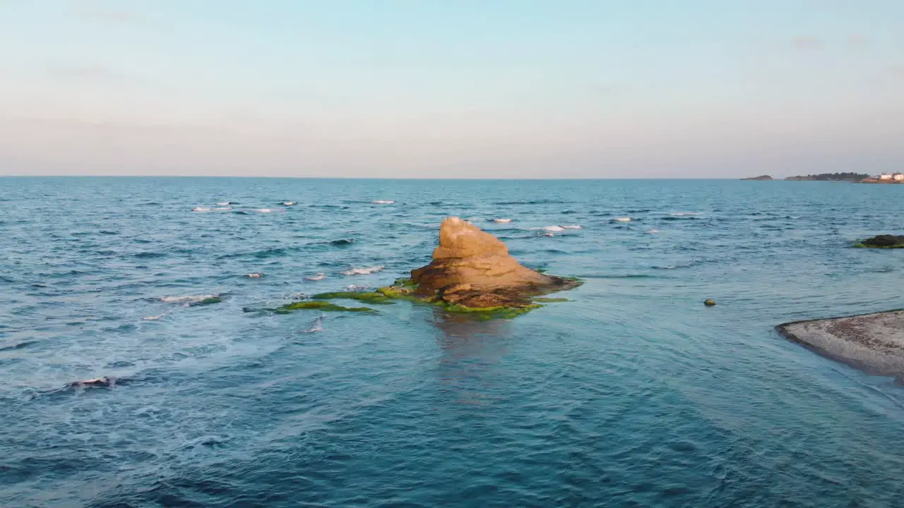 Aerial panning shot around cliff in the sea at sunset-1