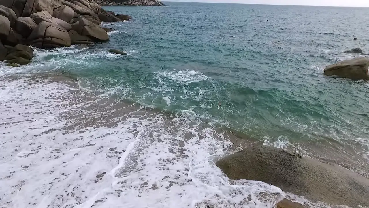 Continuous-wave rushing up to beach over bay at corner side overlook static dronefly shot