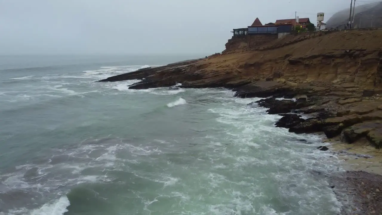 Drone video of a rocky beach shore flying towards a rocky outcrop on a foggy day