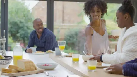 Mother Hands Bowls of Cereal to Two Young Children at Breakfast