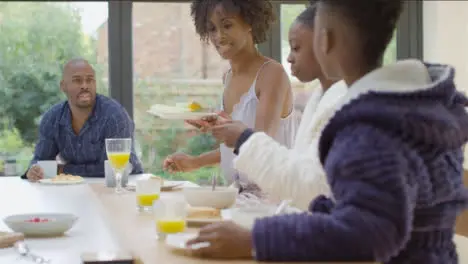 Mother Hands Plate of Sliced Melon to Two Young Children at Breakfast