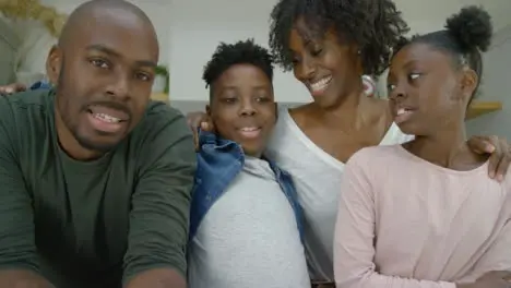 Mother and Father with Two Young Children Talking Directly into Webcam During Video Call