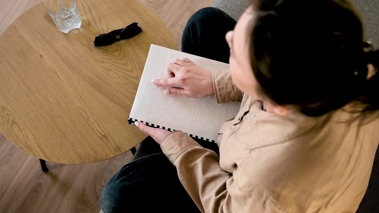 Blinde Frau Liest Ein Braille-Buch Während Sie Zu Hause Auf Dem Sofa Sitzt