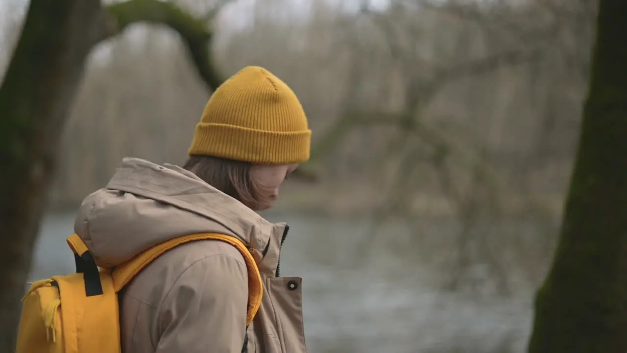 Una Niña En Un Bosque Que Usa Una Gorra De Lana Amarilla Y Una Mochila Amarilla Camina Hacia El Lago