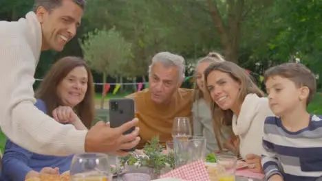 Handheld Shot of Family Talking to Someone Via Phone Video Call During Al Fresco Dinner 01