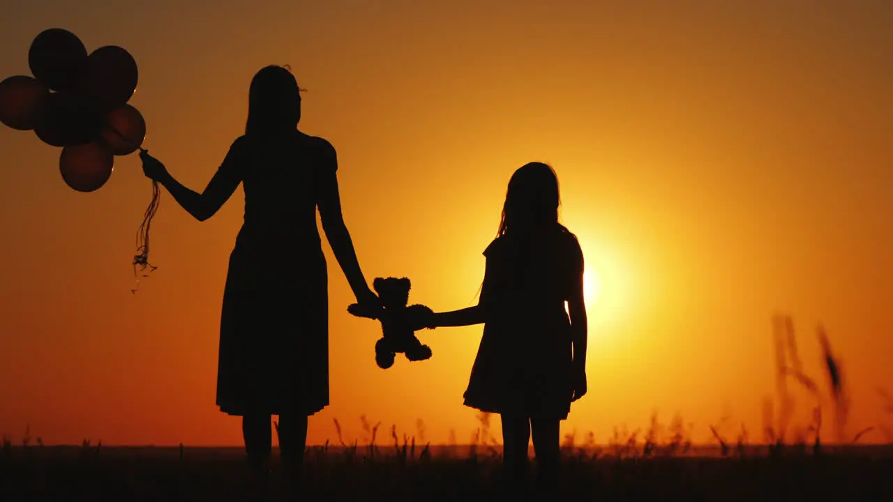 Middle-Aged Woman With Her Daughter Admiring The Sunset Holding A Teddy Bear Together