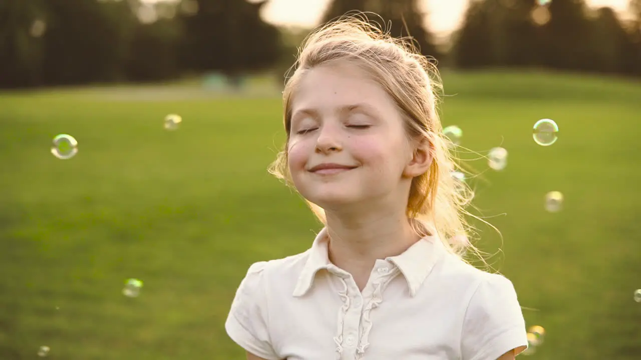 Retrato De Una Linda Niña Rubia Con Los Ojos Cerrados Sonriendo Rodeada De Burbujas De Jabón En El Parque 3