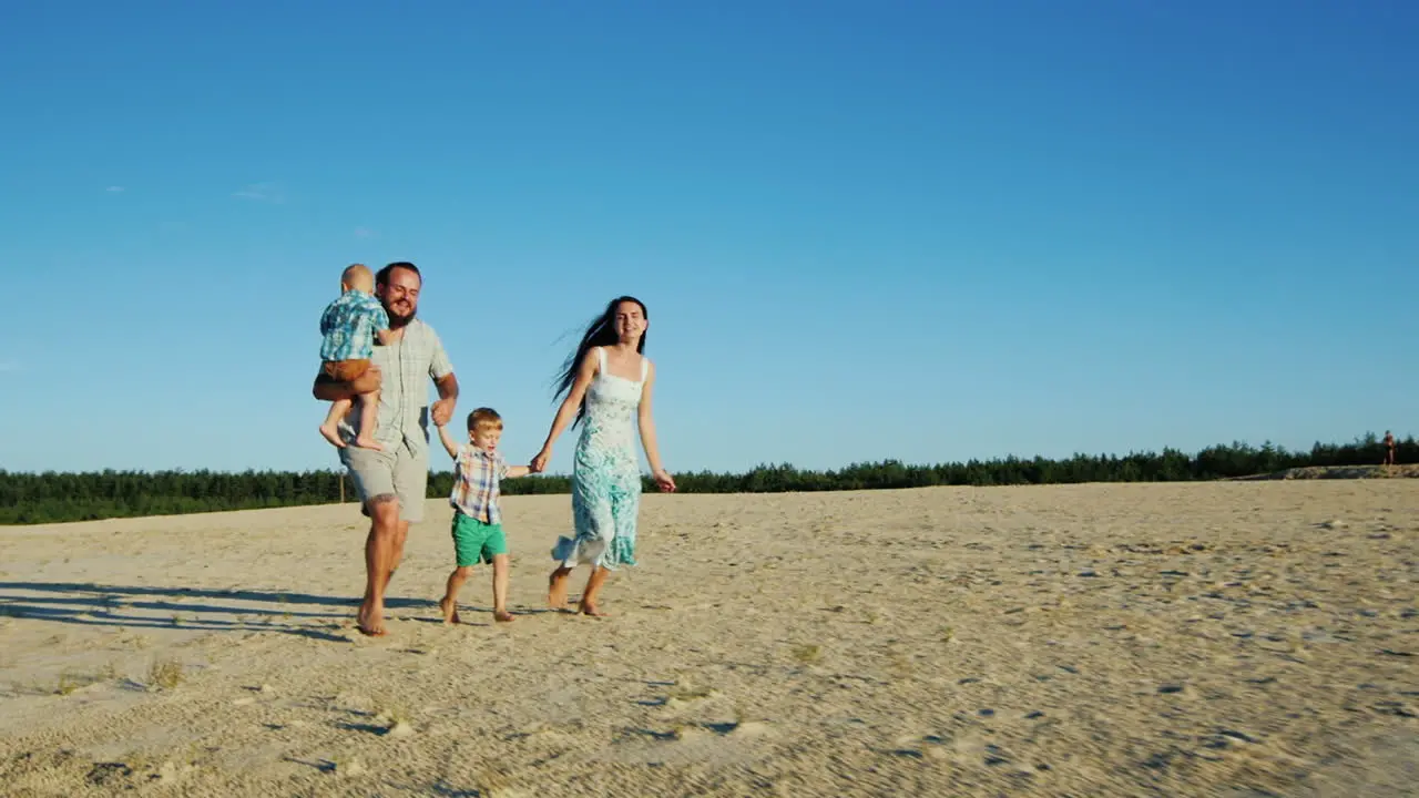 Cheerful Family Running Across The Sand Parents And Two Young Sons