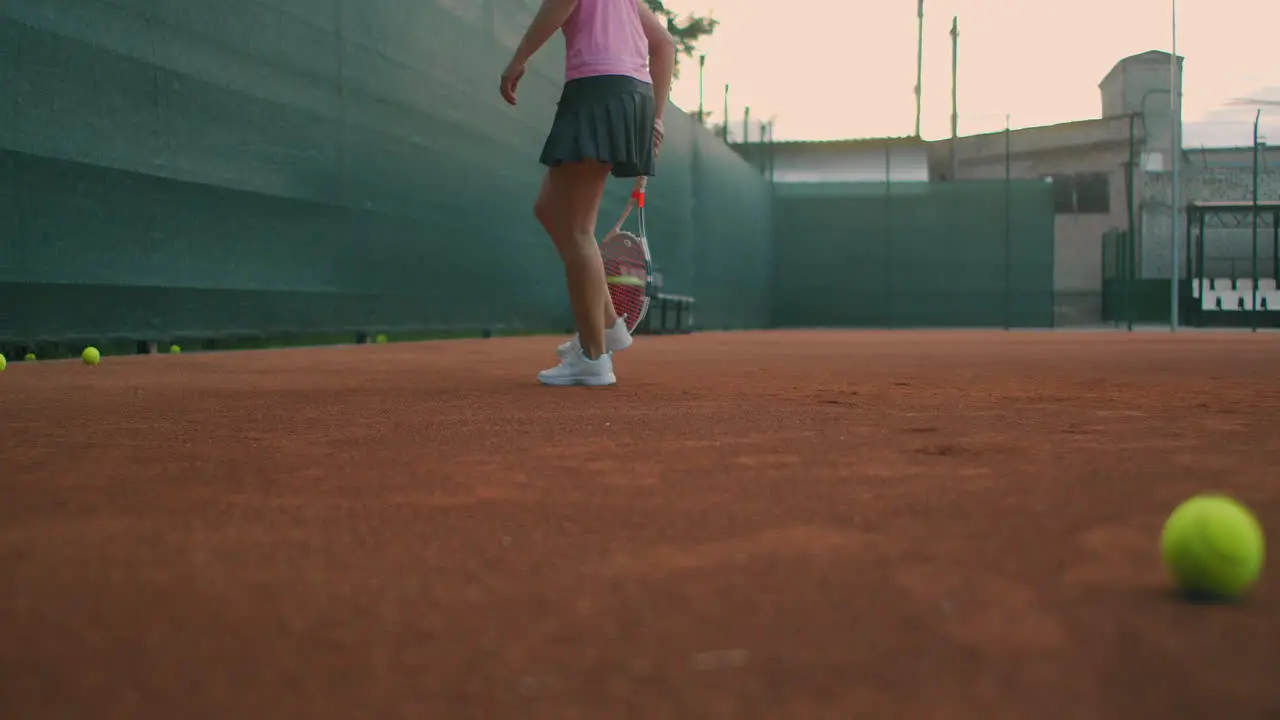 Closeup footage of female legs in sports sneakers and prosthesis on her leg picking up tennis balls from the tennis court ground