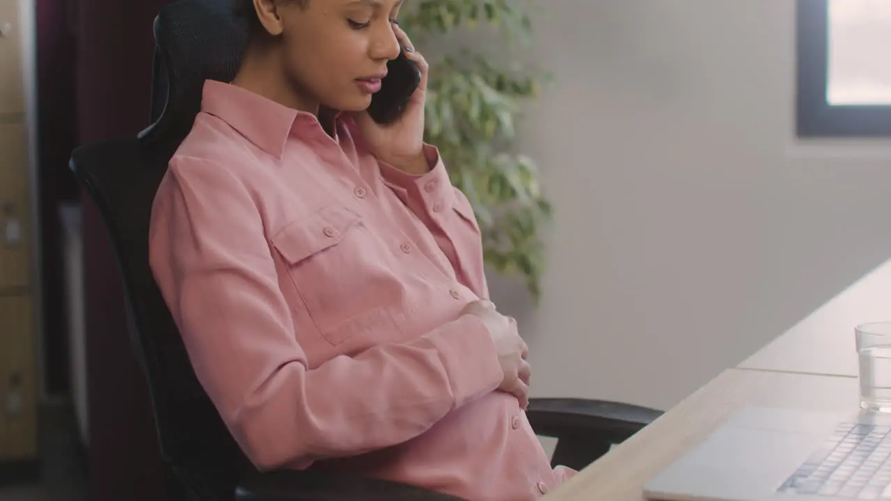 Pregnant Woman Talking On Her Mobile Phone And Caressing Her Belly While Working In The Office 3