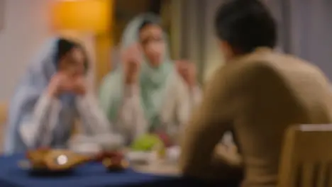 Defocused Shot Of Muslim Muslim Family Sitting Around Table At Home Eating Meal Together