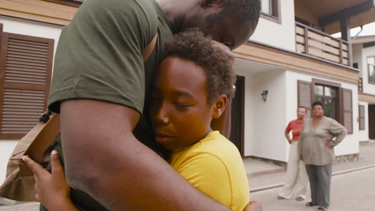 Boy Embracing His Military Father And Saying Goodbye To Him While In The Distance His Mother And Grandma Looking At Them