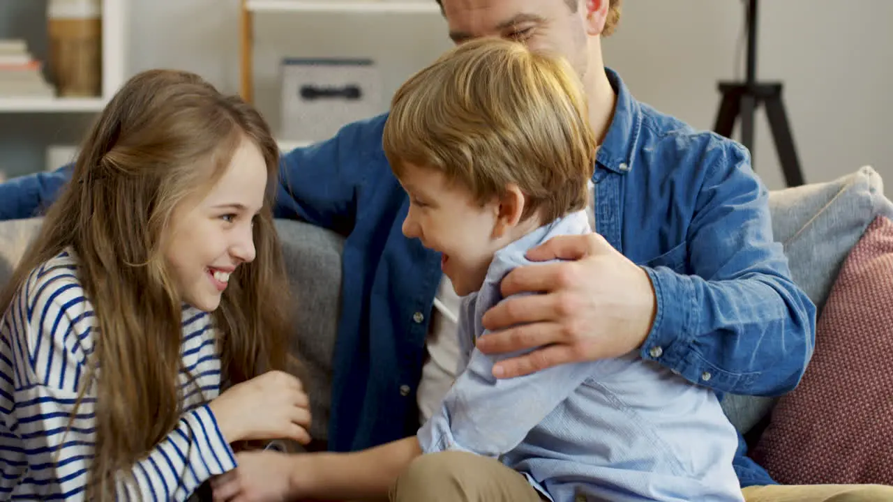 Close Up Of The Little Cute Kids Having Fun On The Sofa In The Living Room Tickling And Laughing While Their Parents Watching Them