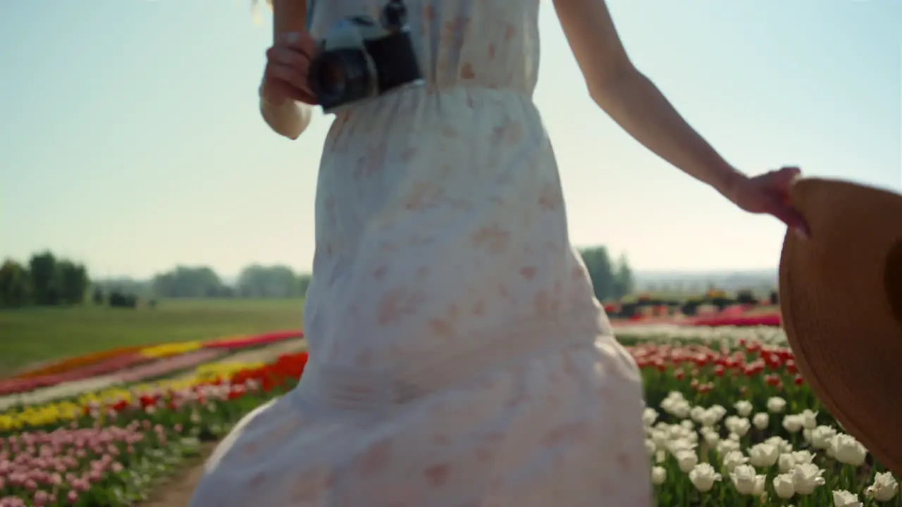 Young woman with camera and straw hat turning around in beautiful tulips garden