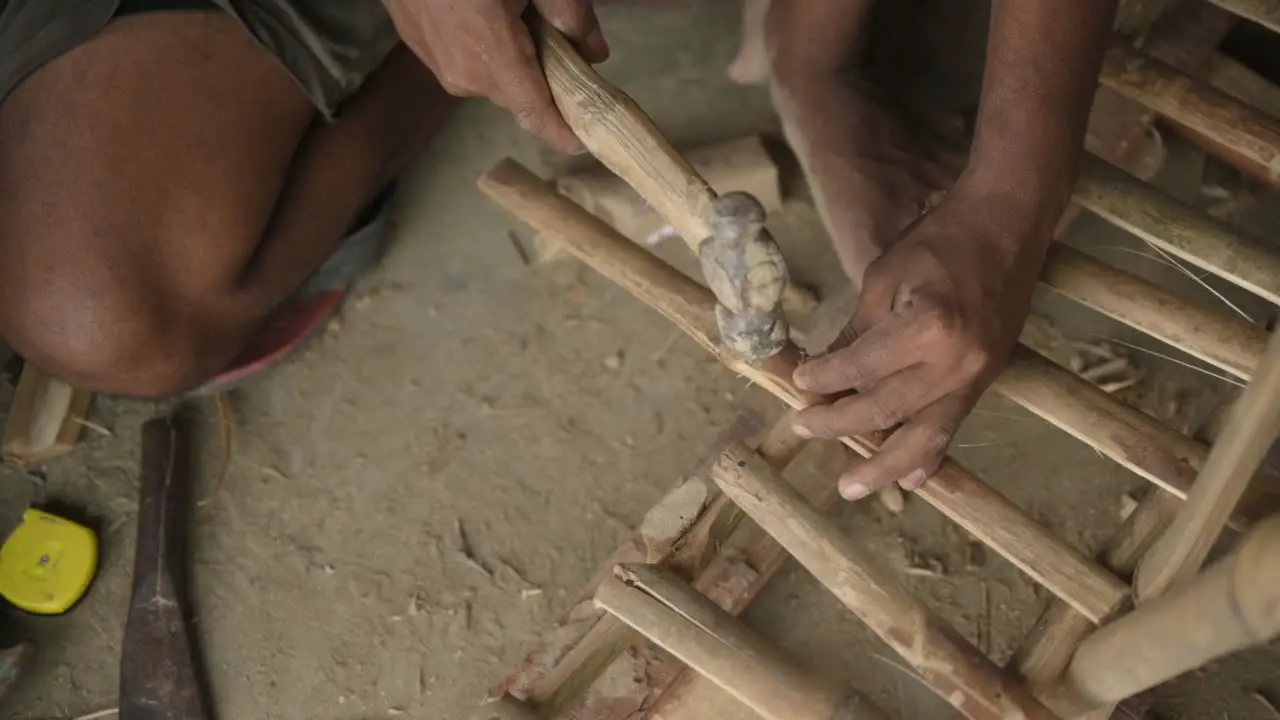 Unrecognized hands of a labour hammering a nail on bamboo sticks slowmotion closeup shot