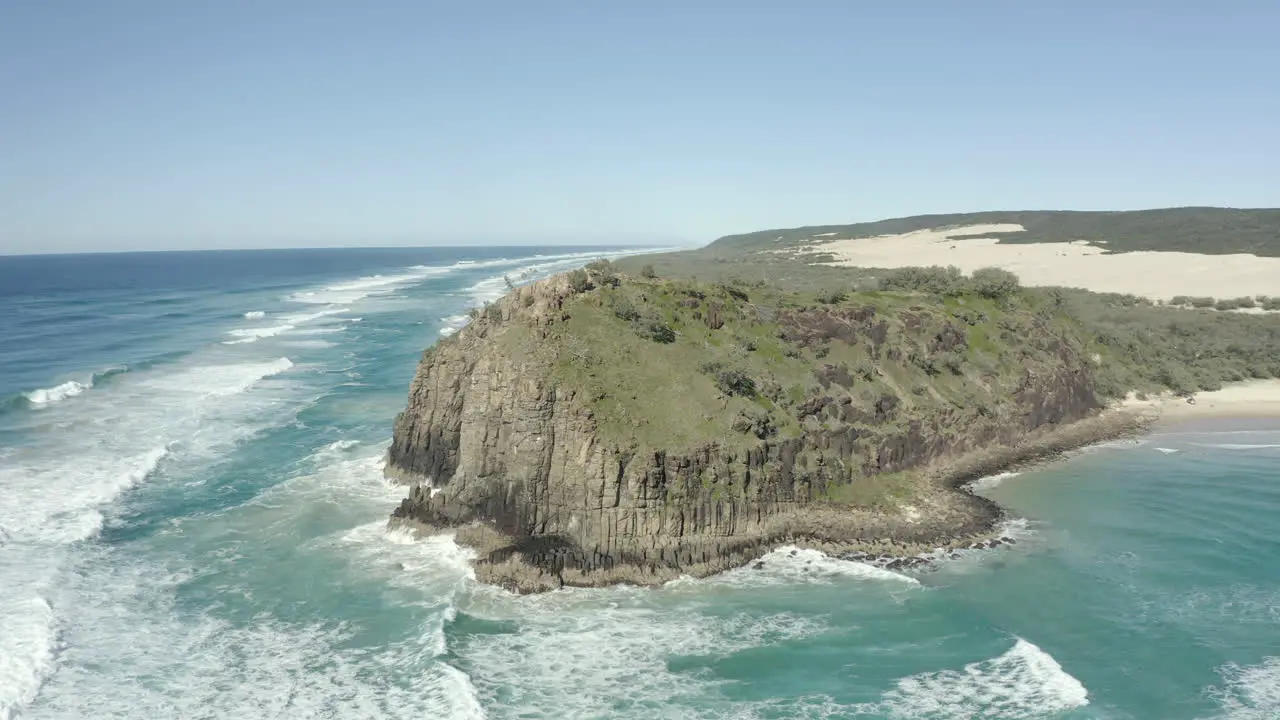 4k drone shot of a mountain cliff next beautiful beach on a clear sunny day on Fraser Island Australia