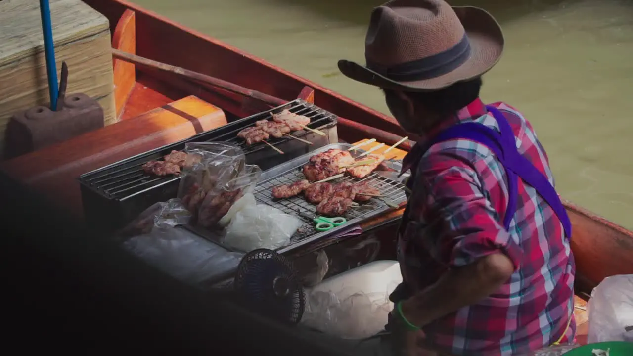 Medium shot Man wearing a cowboy hat rowing a boat Selling Barbeque in Thailand Floating Market