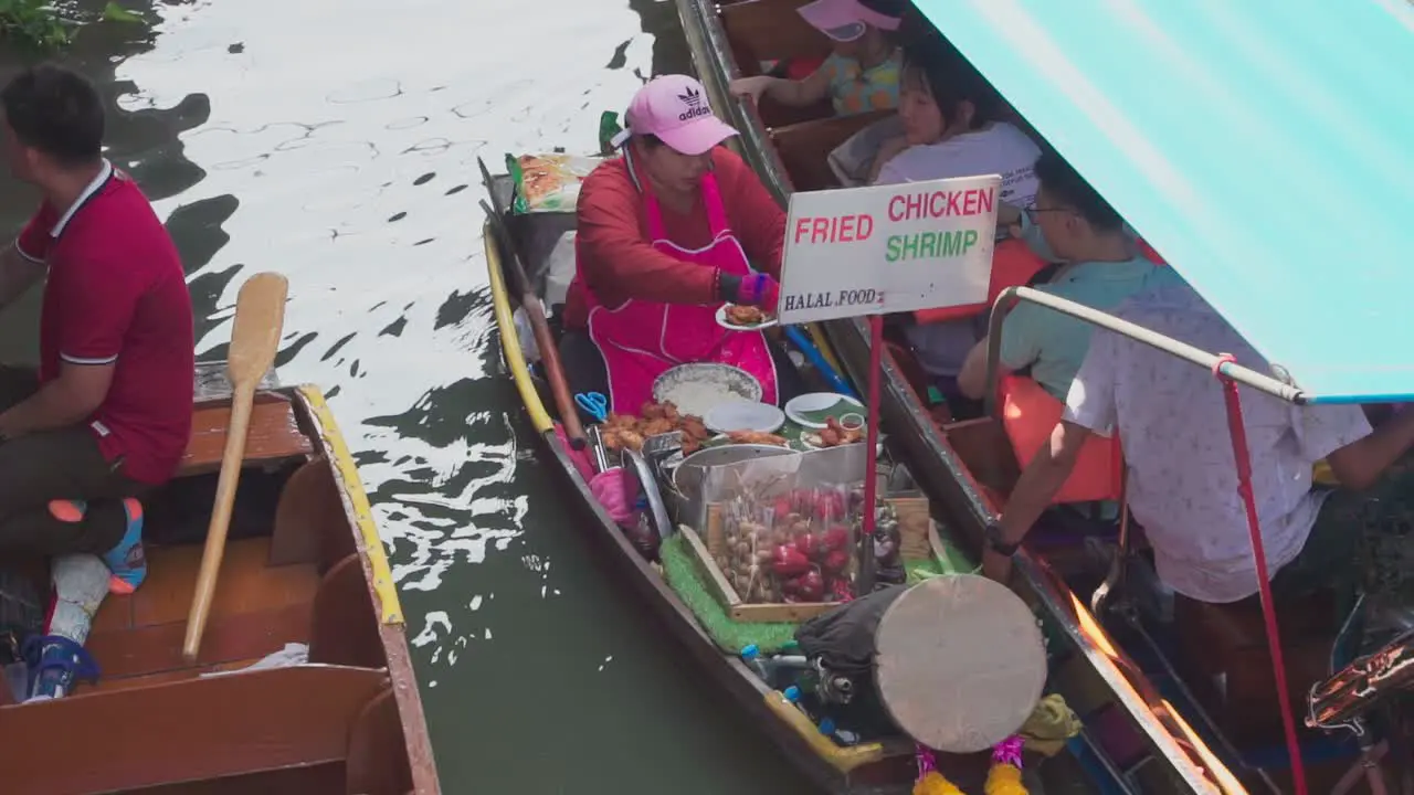 Medium shot Women in pink apron selling fried chicken and shrimp to tourist in Thailand Floating Market