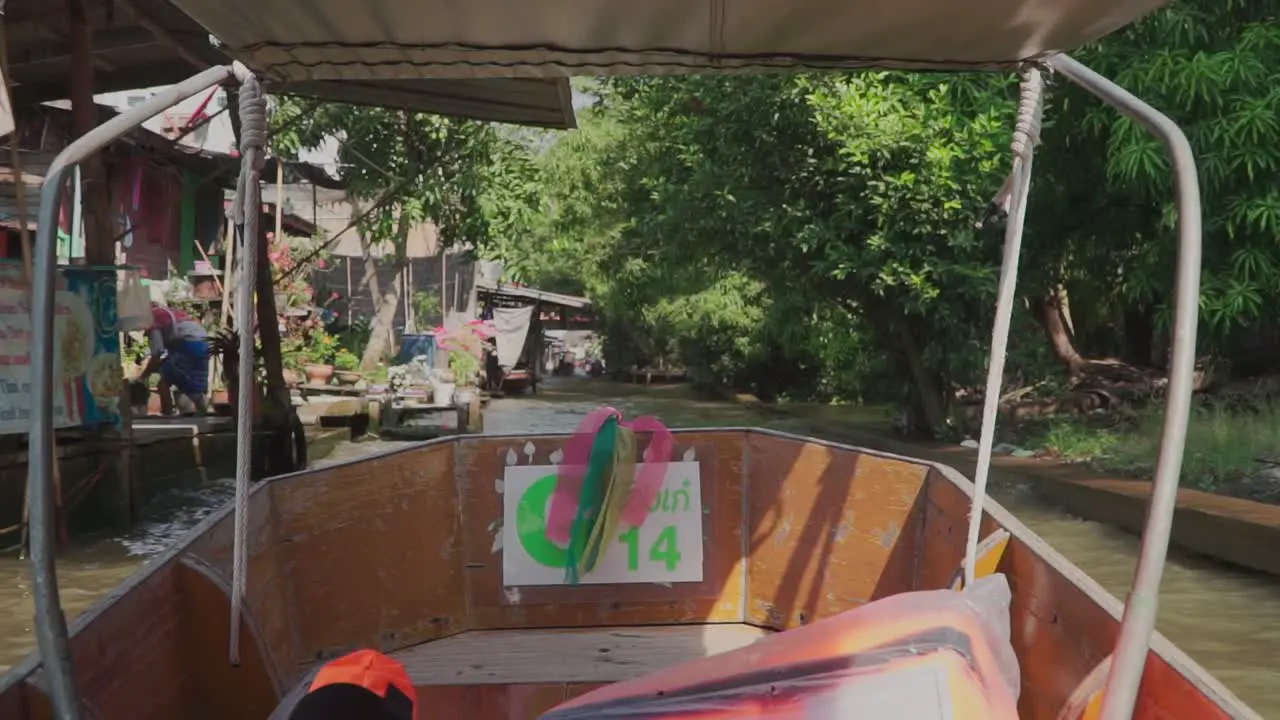 Moving Forward shot Inside the wooden boat in the Damnoen Sudoku River Shops and Houses along the river in the background