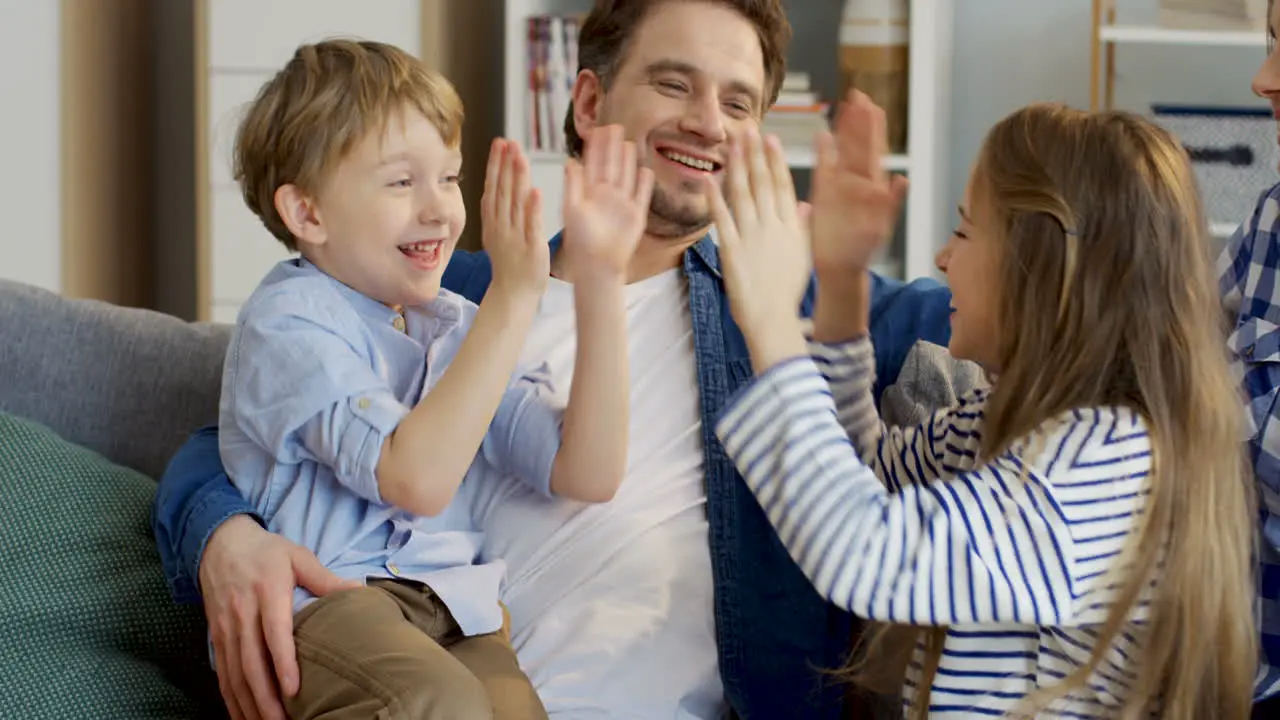 Joyful Small Children Boy And Girl Sitting On The Knees Of Their Parents And Playing A Hand Game