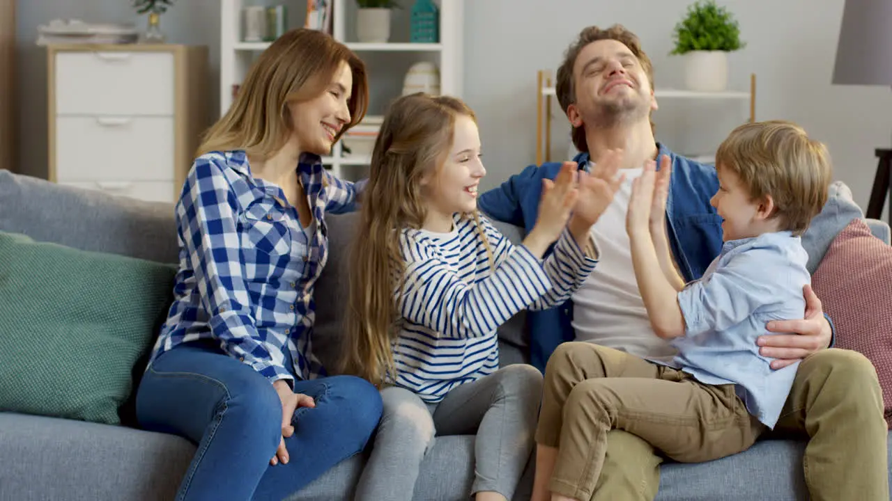 Cute Little Kids Boy And Girl Sitting On The Knees Of Their Mother And Father And Playing A Hand Game