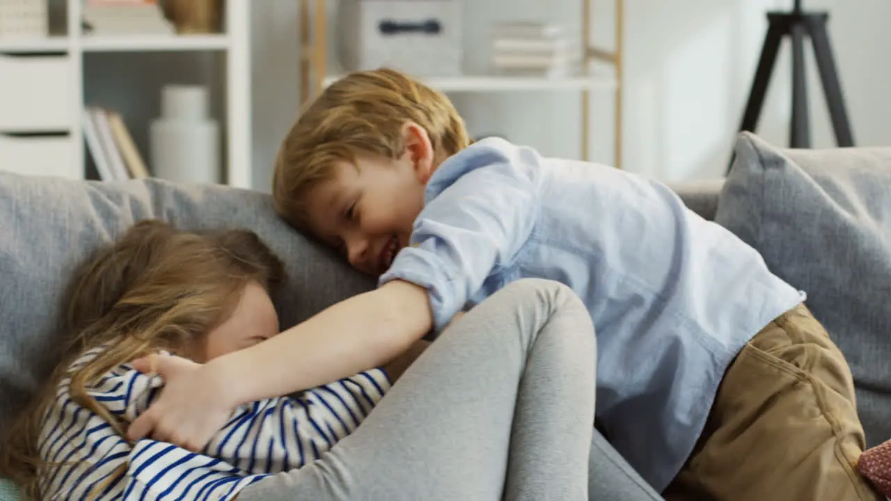 Two Little Funny Kids Boy And Girl Having Fun On The Couch In The Cozy Room Tickling And Laughing