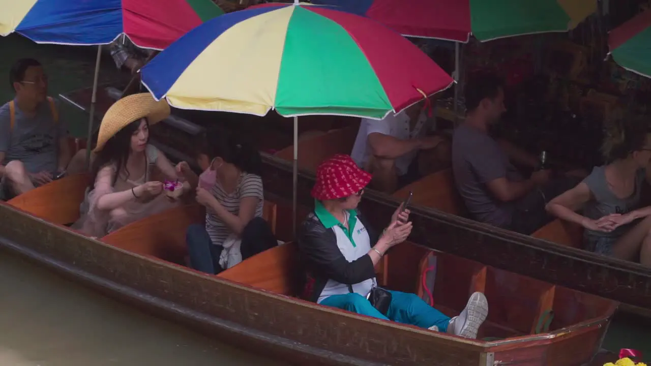 Establishing Shot Wooden boat with colorful umbrella tourist takes photos in Thailand floating Market Tourist Boat Park near the market in the background