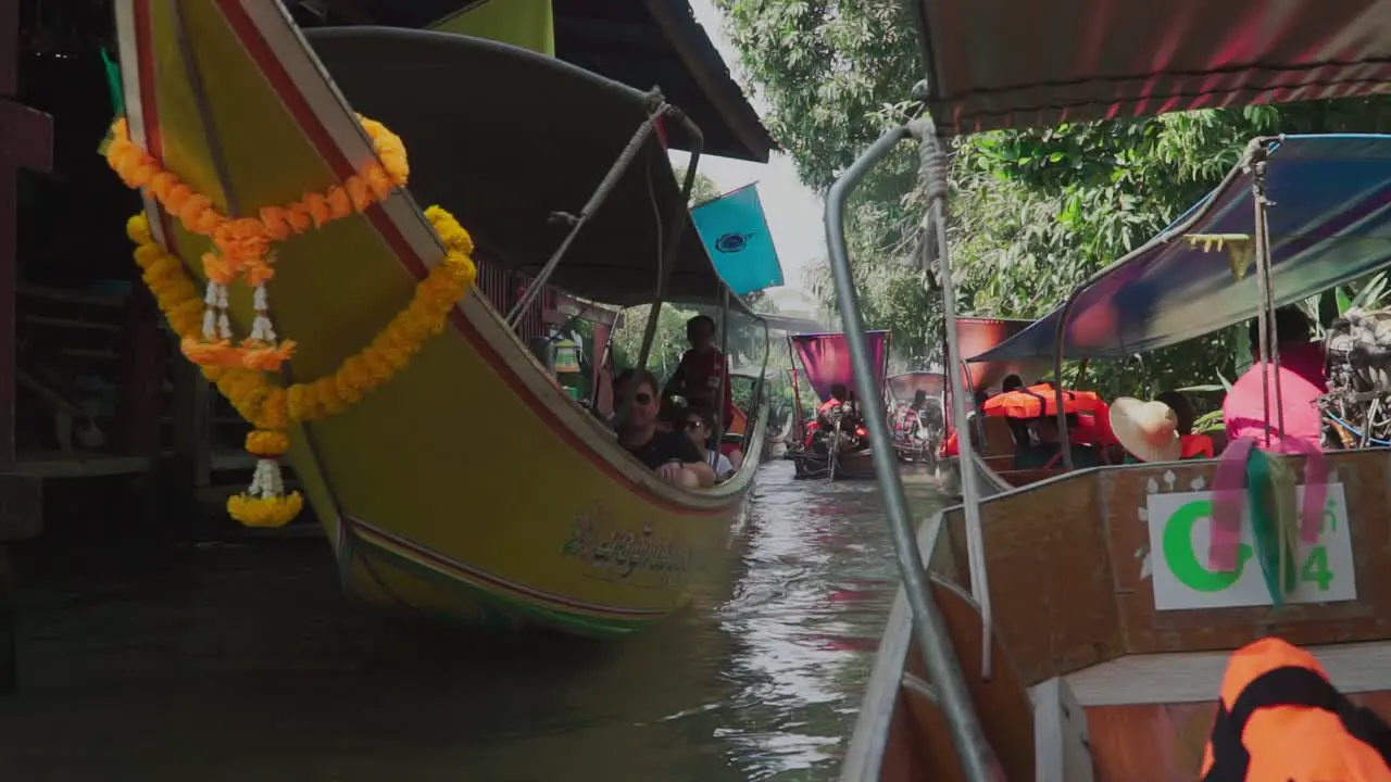 Establishing shot boat with tourists passing by and waving with peace sign in Thailand Floating Market pump boat fall in line in the background