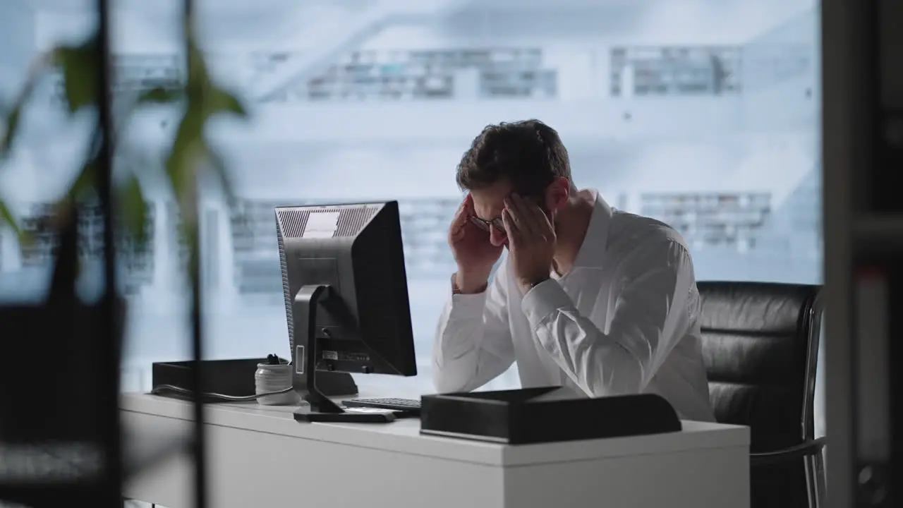 Man sit indoor closed eyes rub temples suffering from headache Stressed young man in glasses suffering from muscles tension having painful head feelings due to computer overwork or sedentary working