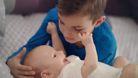 Siblings have fun on bed Boy playing with baby Older brother care infant