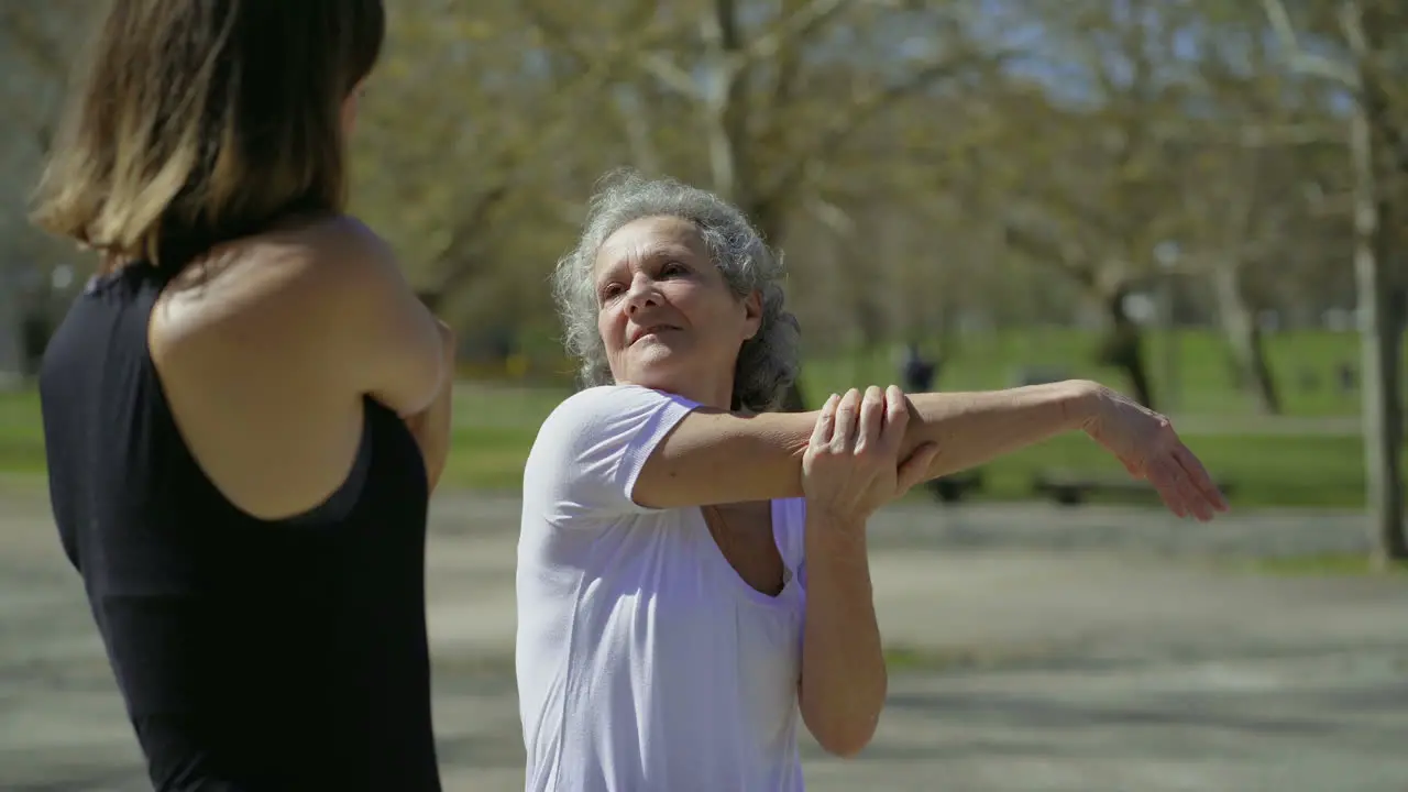 Sporty senior and young women stretching arms and talking in park