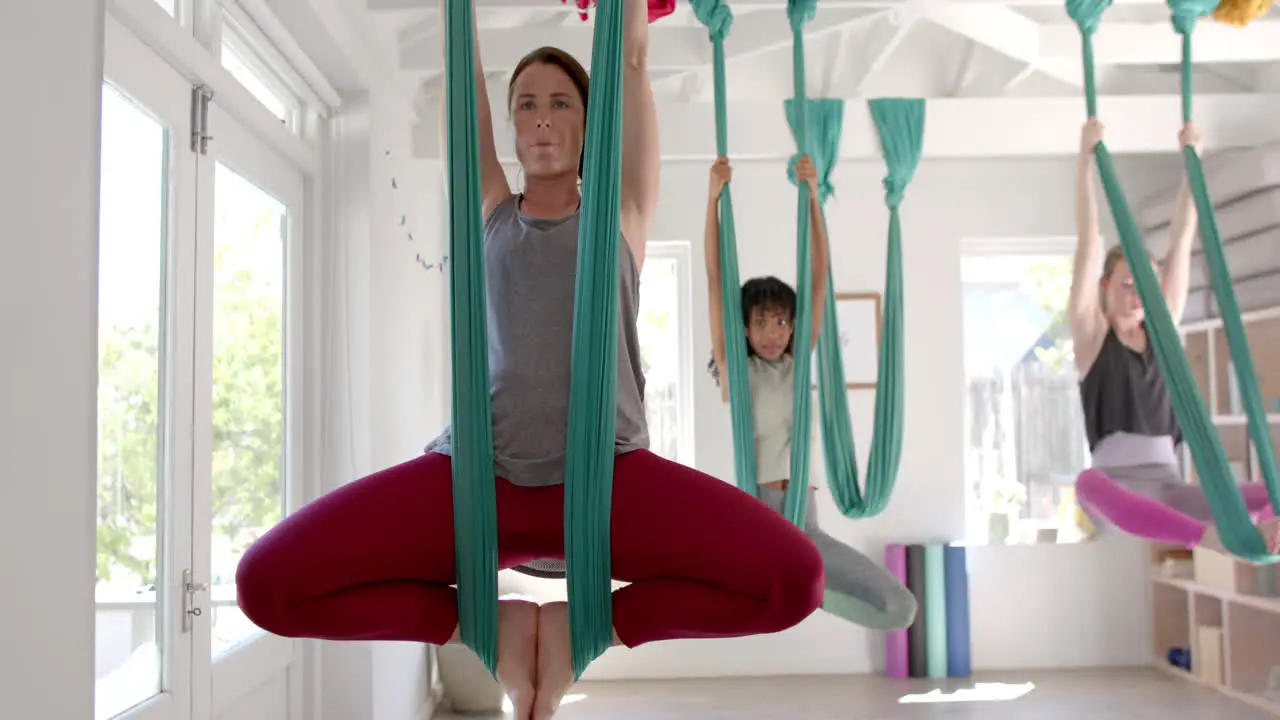 Focused diverse fitness women exercising in aerial yoga class in big white room slow motion