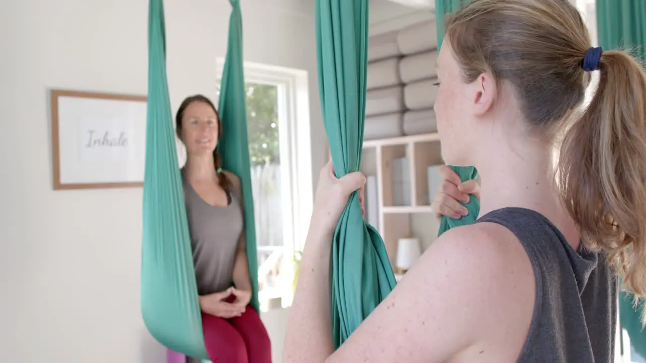 Diverse fitness women exercising in aerial yoga class in big white room slow motion