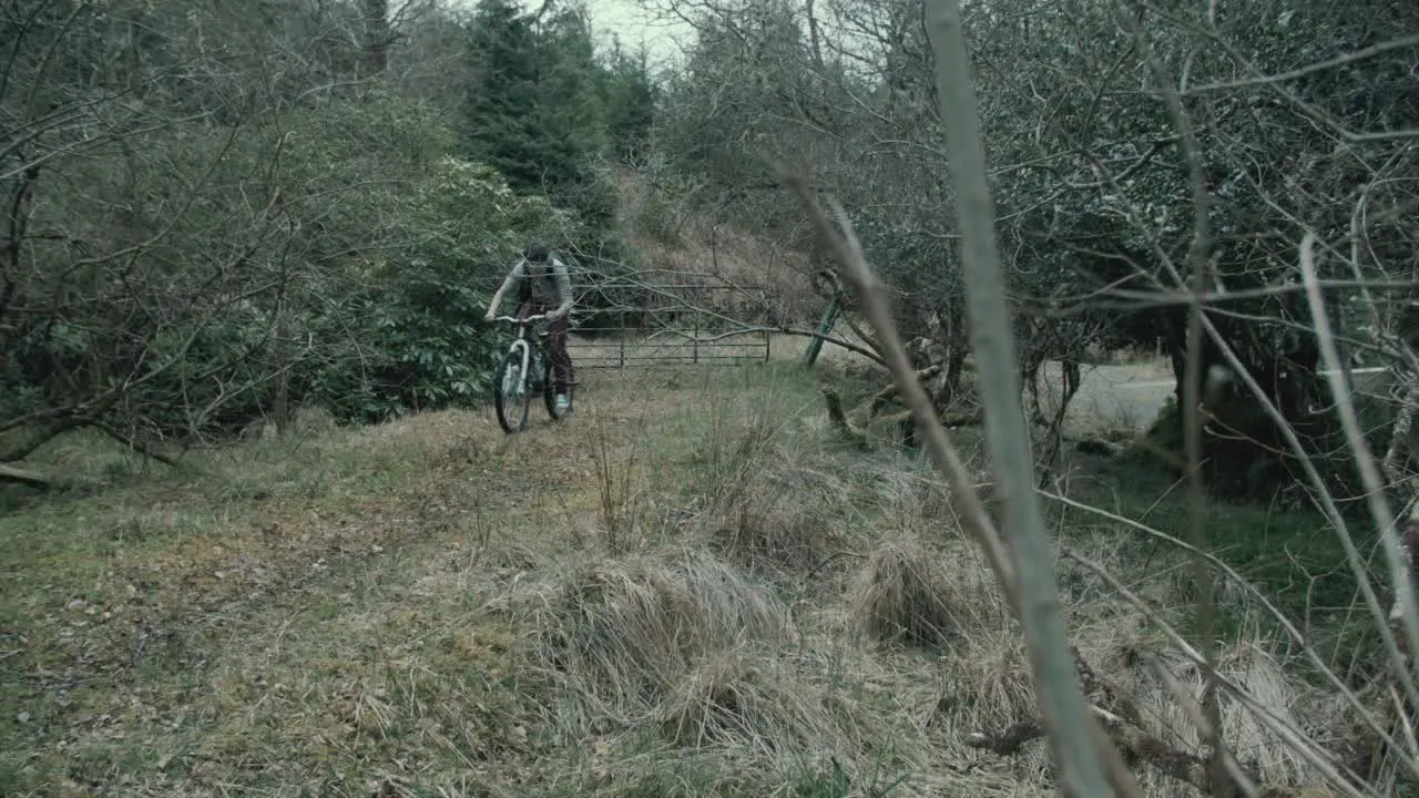 Filmmaker cycles within forest with backpack and tripod