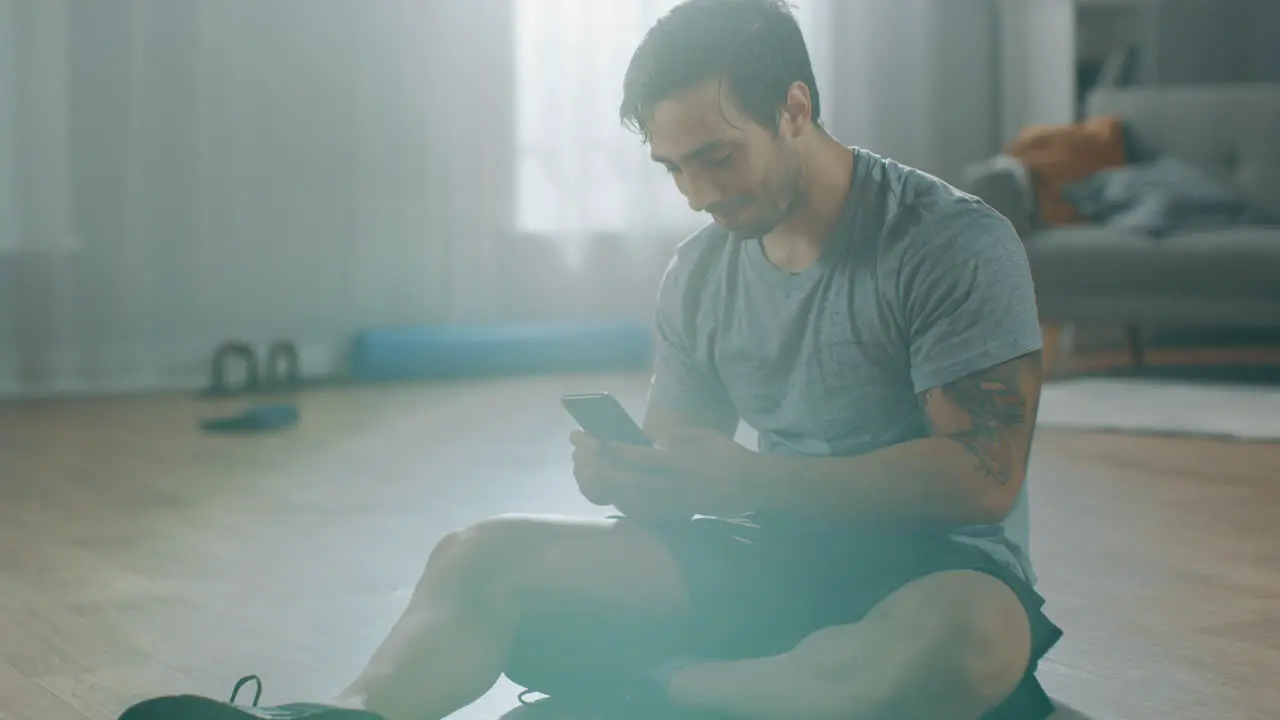 Fitness man taking a break from his work out and he is reading the messages on his phone