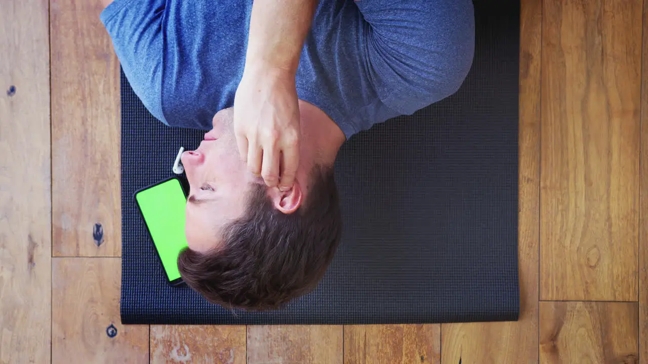 Overhead View Of Man Lying On Exercise Mat At Home Putting In Wireless Earphones