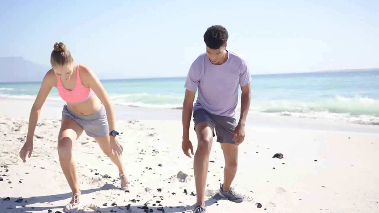 Young Caucasian woman and biracial man are ready to sprint on a sunny beach