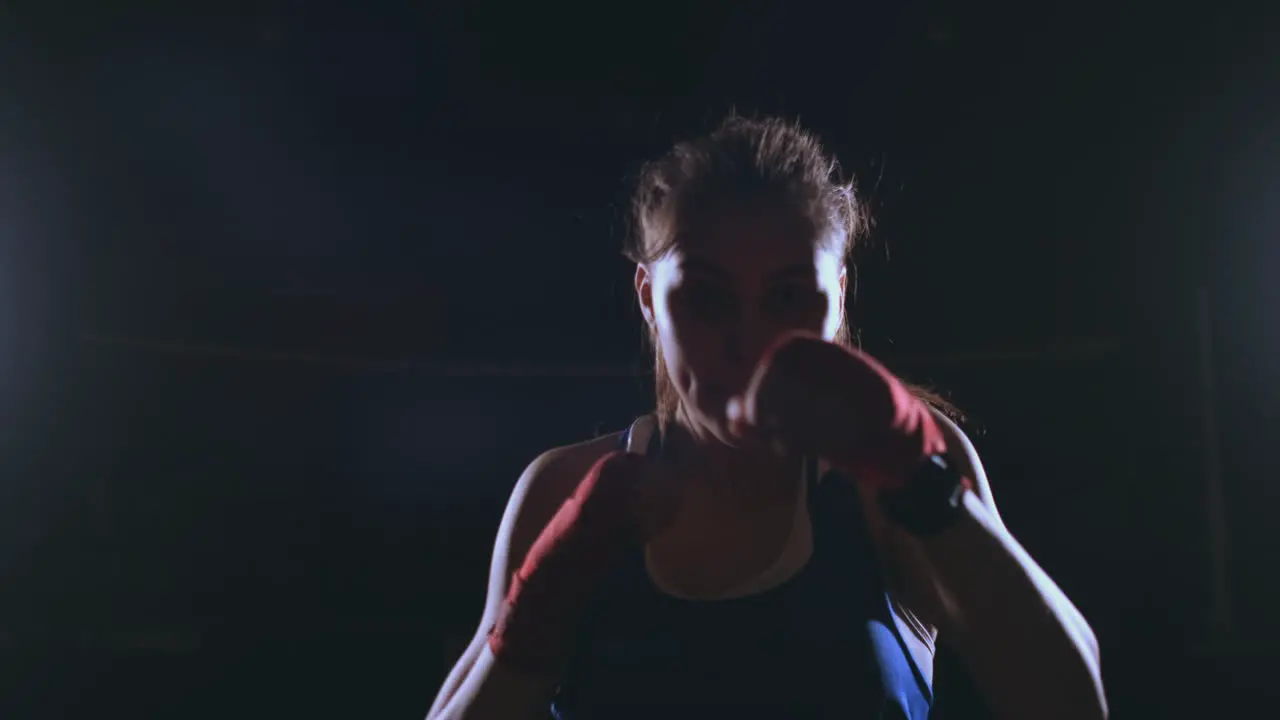 Beautiful sexy woman boxer dynamically strikes directly into the camera and moving forward on a dark background with a backlight Steadicam shot