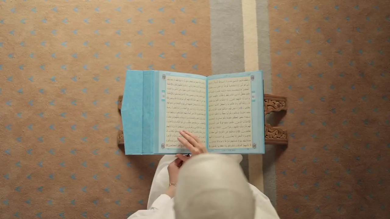 Overhead shot of hijabi woman reading Quran from mushaf on stand